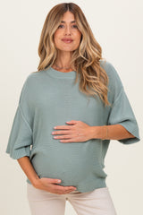 woman wearing a light green maternity sweater and holding her baby bump