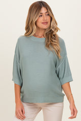 woman wearing a light green oversized maternity sweater with rolled sleeves and a visible baby bump