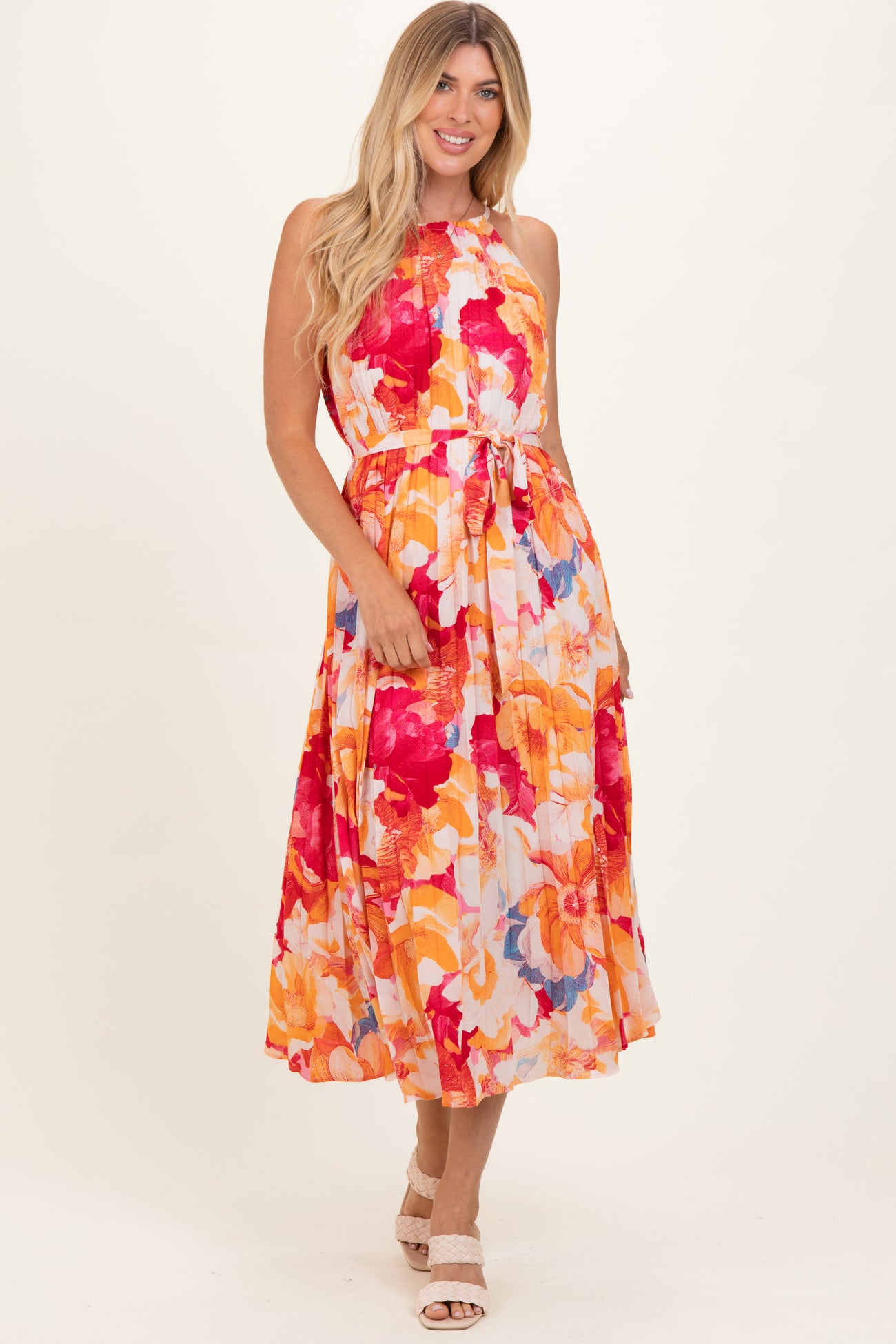 woman wearing a floral maxi dress with a tie waist in vibrant shades of orange, pink, and red.