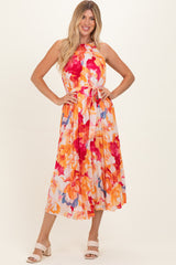 woman wearing a sleeveless floral midi dress with orange, pink, and purple flowers and a tie waist detail