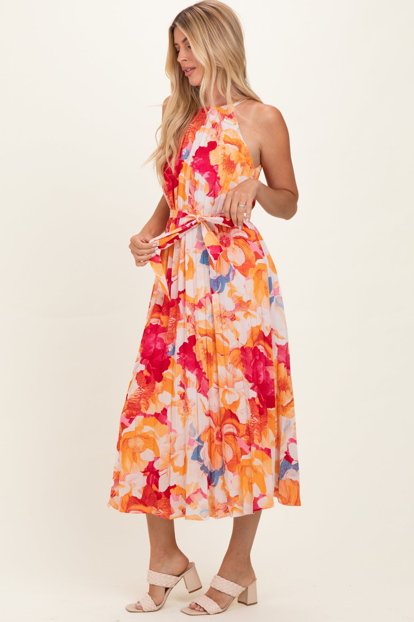 woman wearing a floral halter neck maxi dress with bright orange, pink, and blue tones.