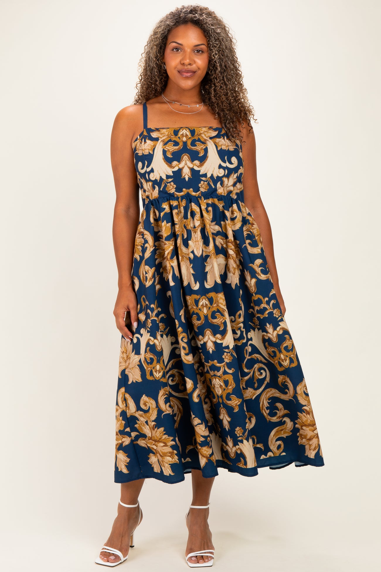 woman wearing a navy blue plus size maxi dress with gold floral patterns and spaghetti straps
