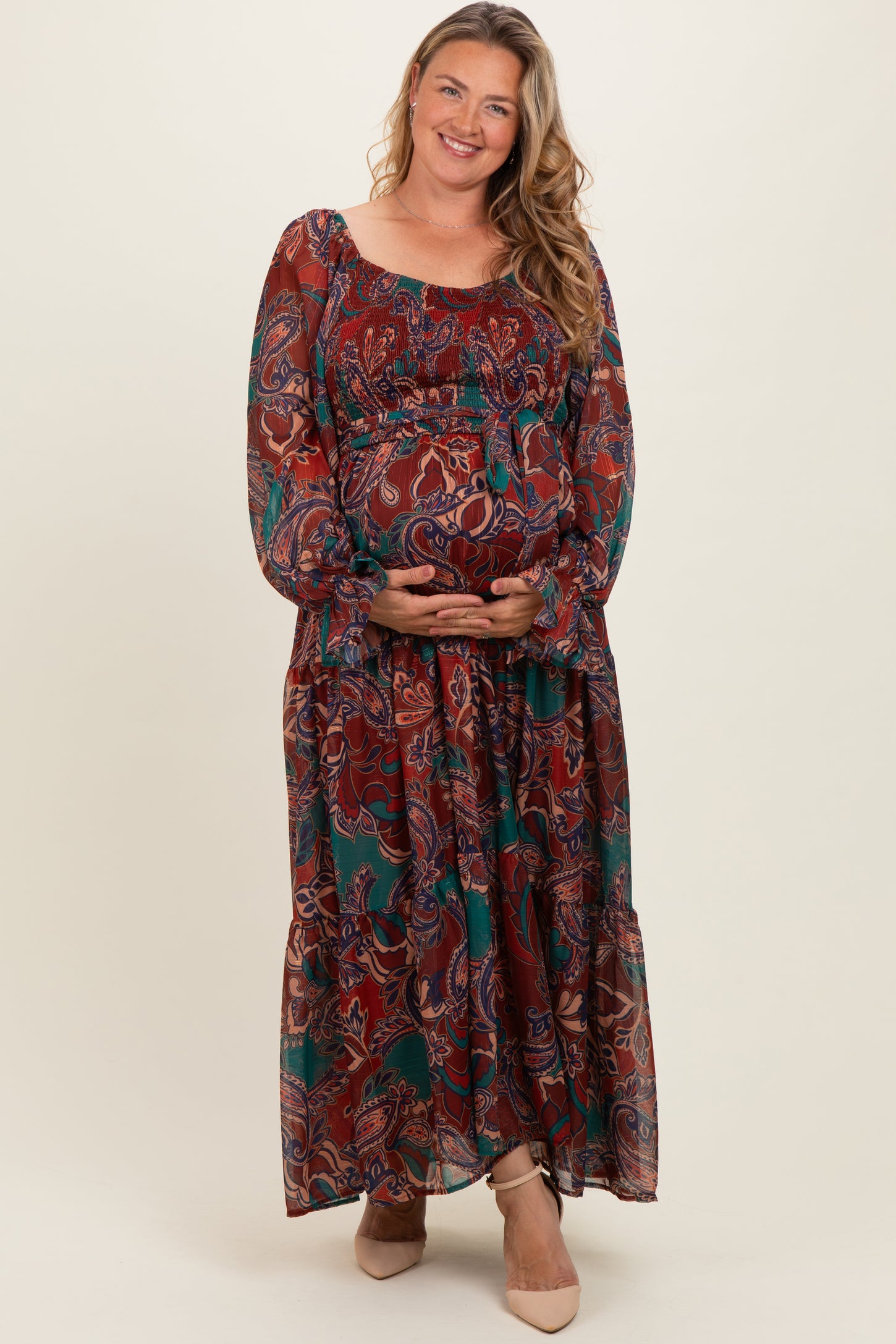 woman wearing a bohemian style maternity plus maxi dress with floral patterns and holding her baby bump