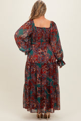 woman wearing a long sleeve red and green paisley print maternity maxi dress with a tiered hemline and a flowy silhouette