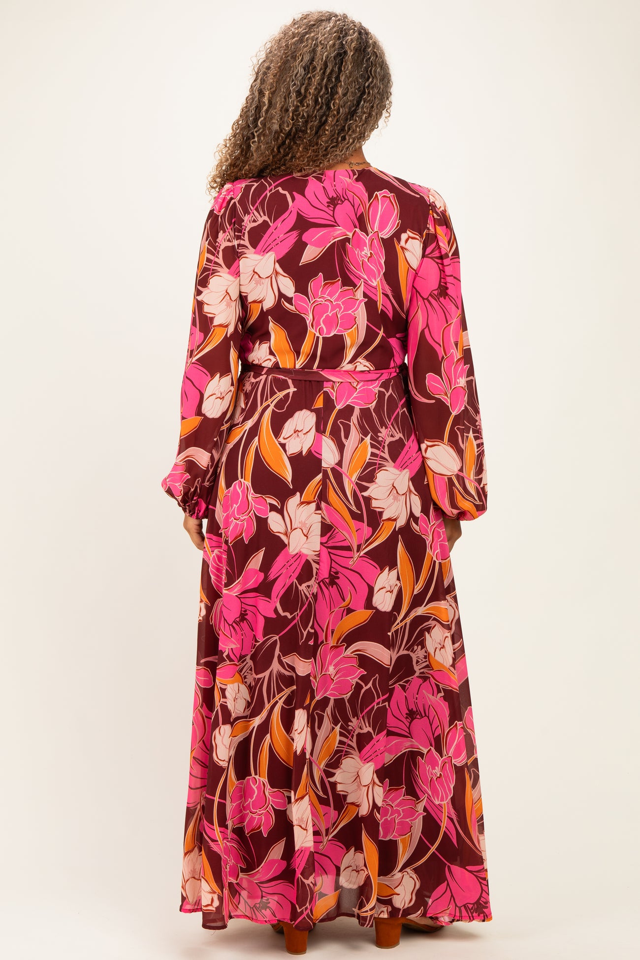 woman wearing a floral maxi dress in shades of pink, maroon, and orange with long sleeves and a cinched waist