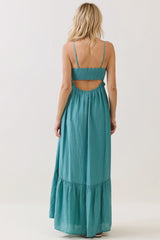 woman wearing a teal backless maxi dress with adjustable straps and a tiered skirt