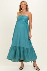 woman wearing a teal maternity maxi dress with a knot detail and tiered hem, showcasing her baby bump