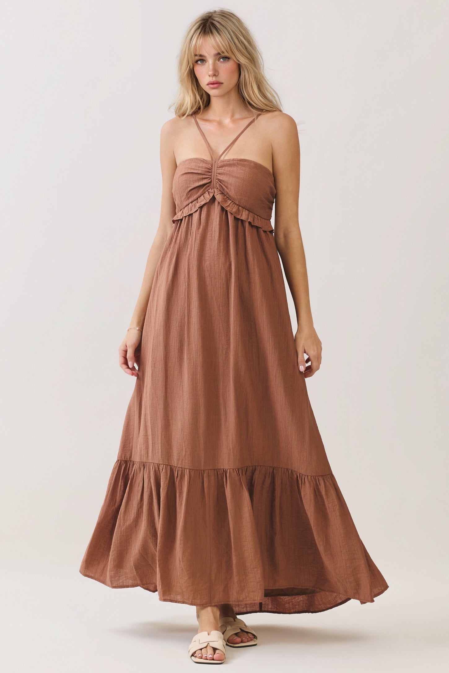 woman wearing a brown maxi dress with a ruffled bodice and spaghetti straps, standing against a neutral backdrop