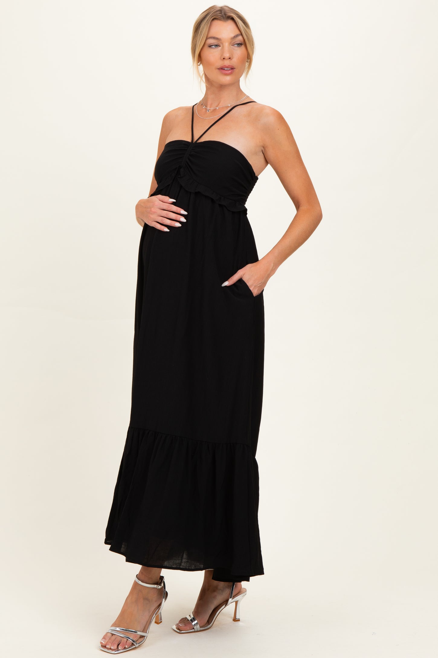 woman wearing a black strapless maternity maxi dress with a tiered hem and side pockets, showing her baby bump