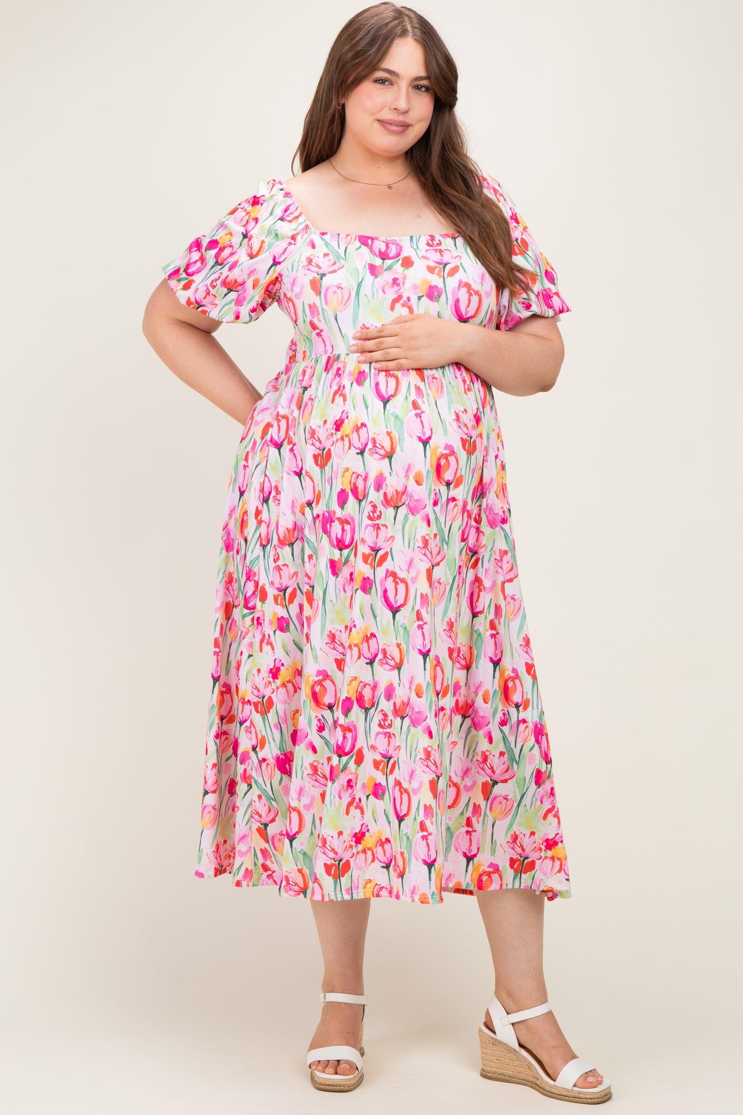 woman wearing a floral maternity plus dress with short puff sleeves and holding her baby bump