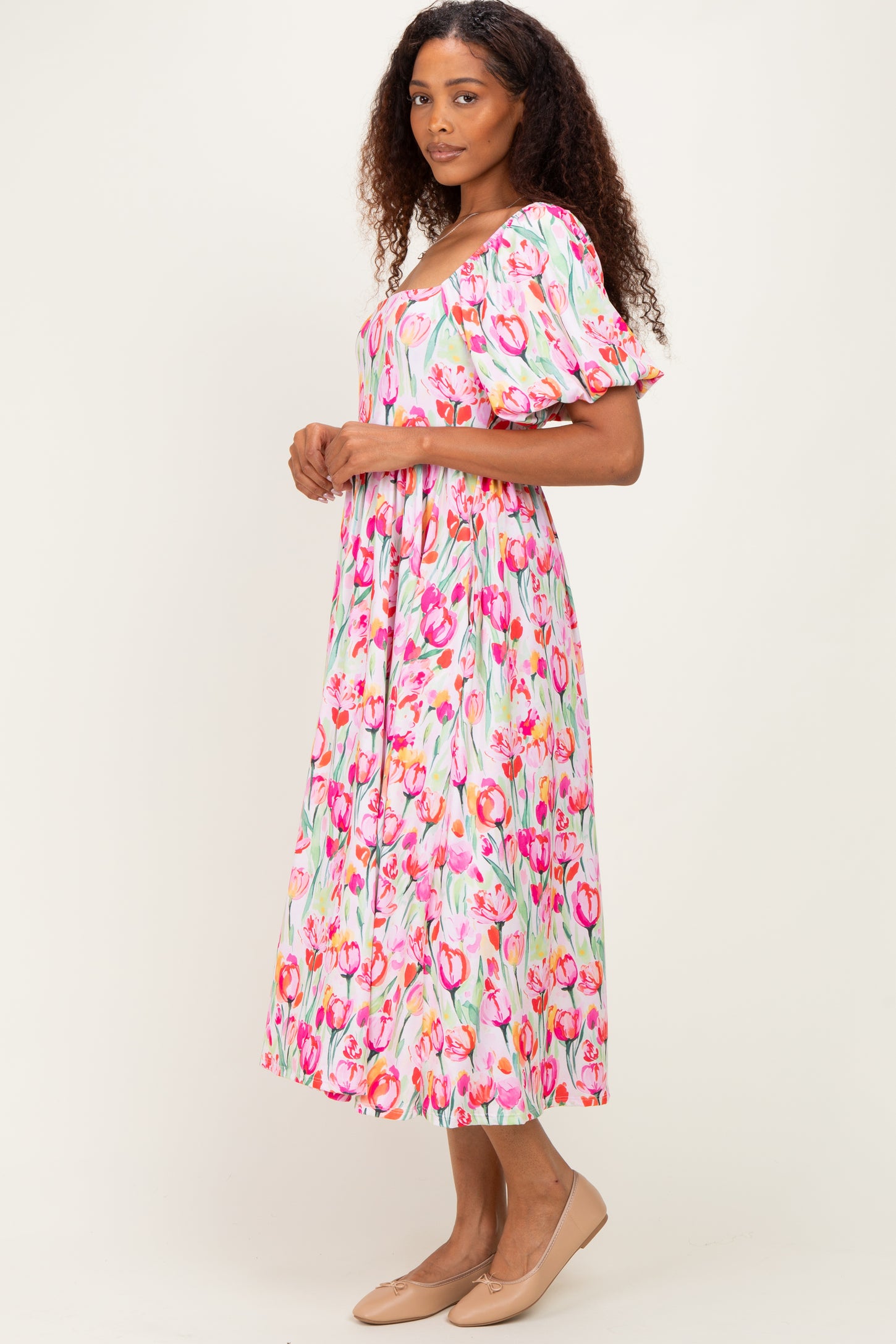 woman wearing a floral midi dress with puff sleeves and a square neckline in shades of pink and green