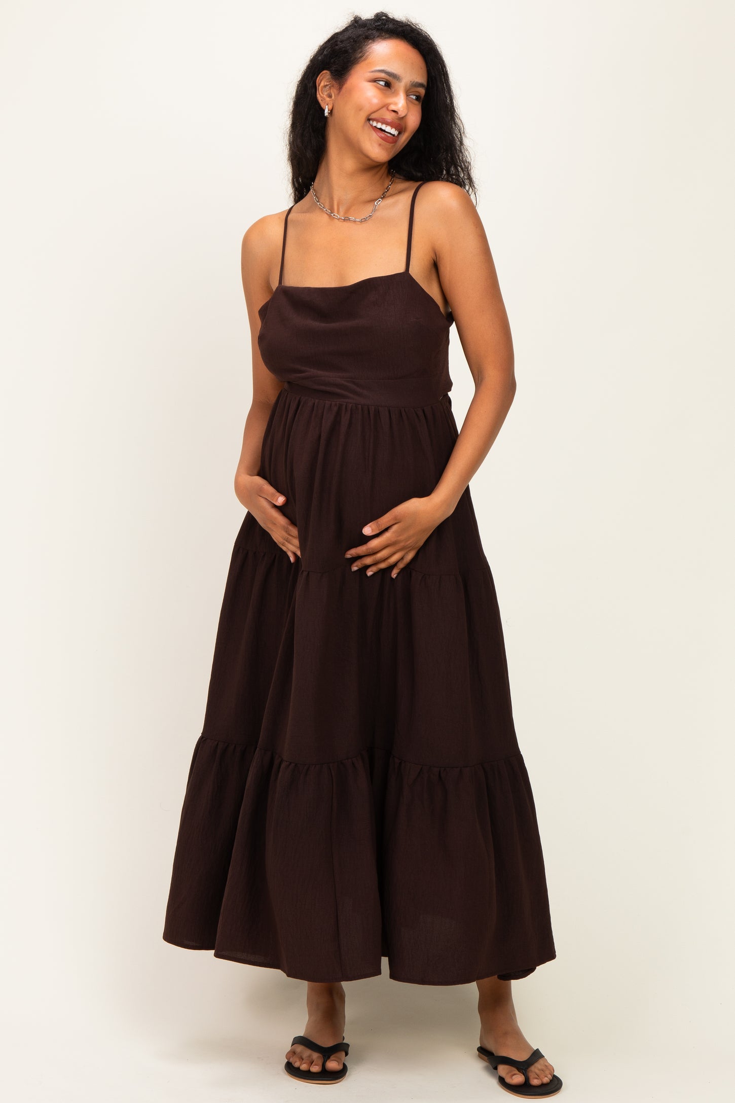 woman wearing a brown tiered maternity maxi dress and holding her baby bump