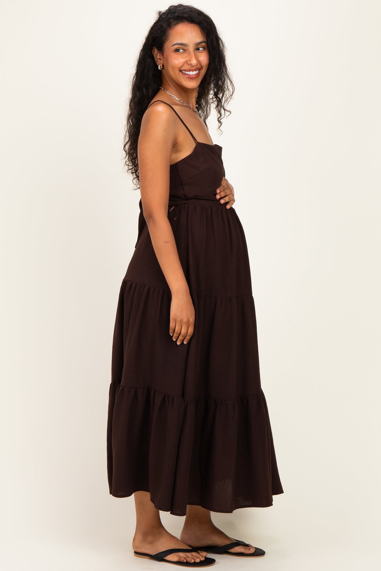 woman wearing a brown tiered maternity dress and holding her baby bump