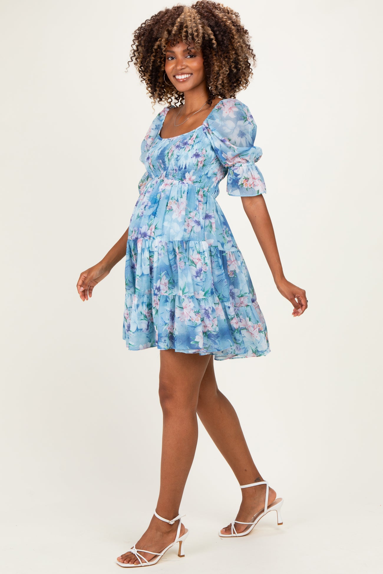 woman wearing a light blue floral maternity dress with puff sleeves and a flowing silhouette, showcasing her baby bump