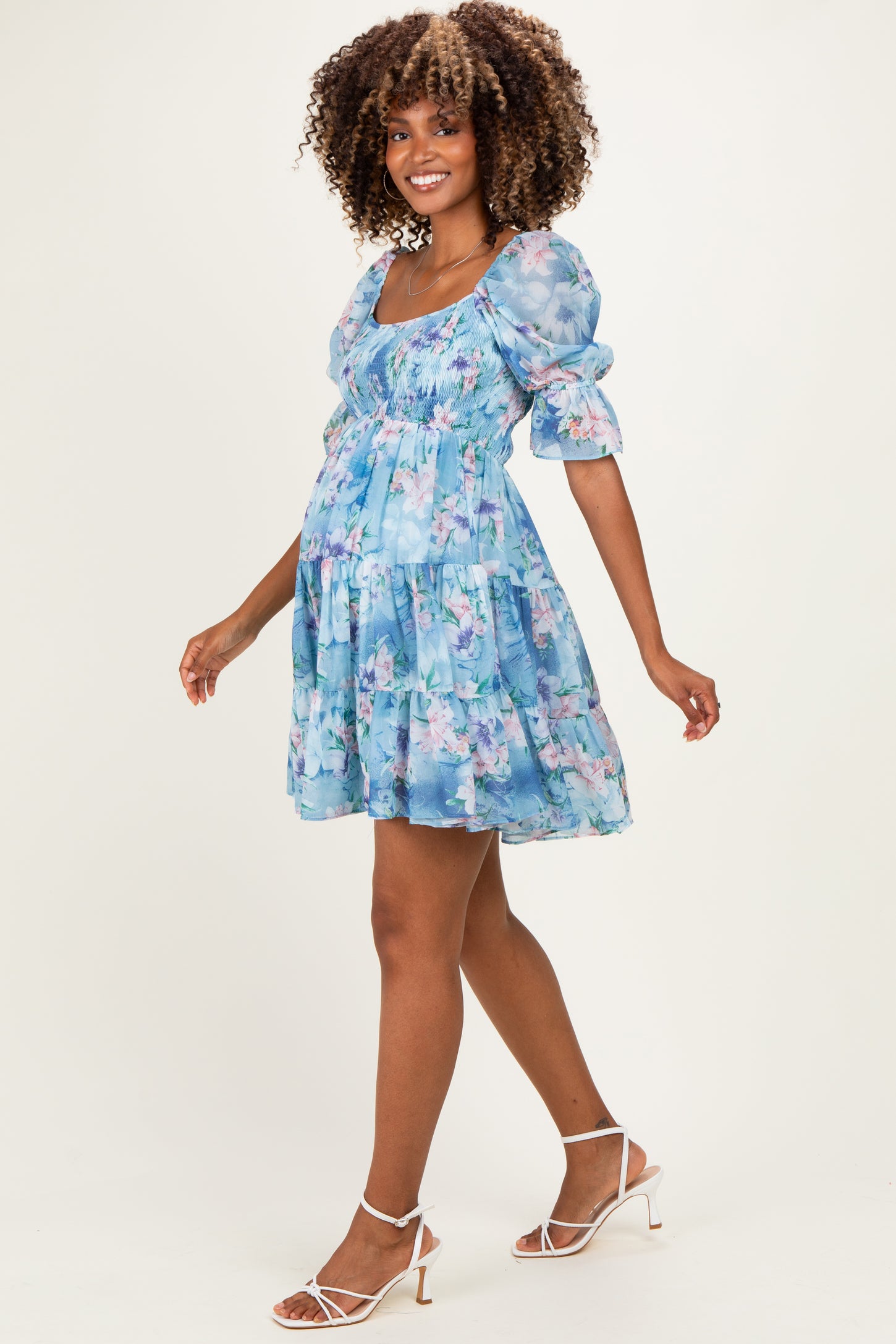 woman wearing a light blue floral maternity dress with puff sleeves and a flowing silhouette, showcasing her baby bump