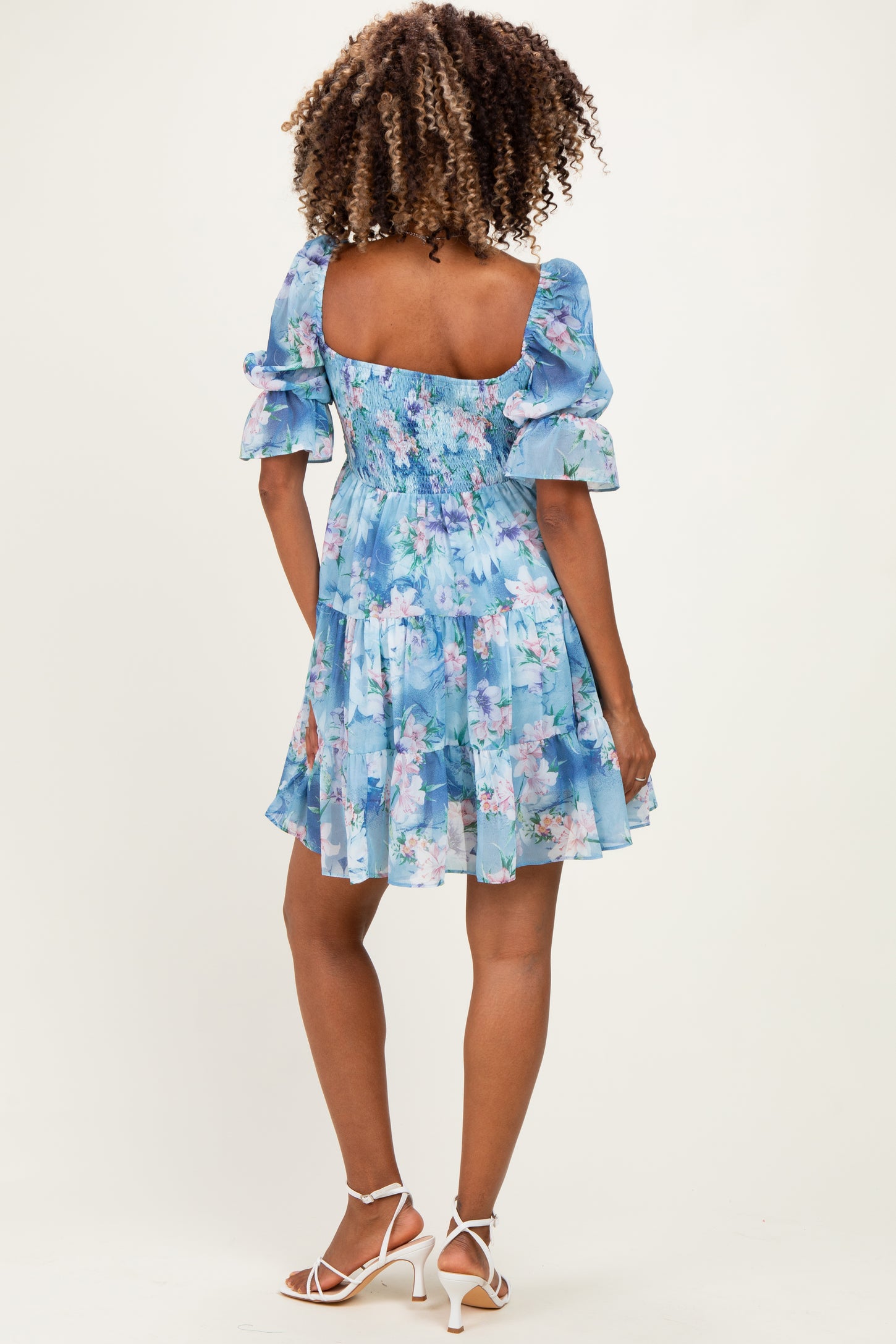 woman wearing a light blue floral maternity dress with puff sleeves, showing a baby bump from the back