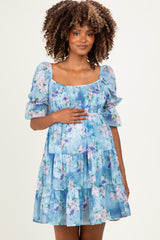woman wearing a light blue floral maternity dress with puff sleeves and tiered ruffles, showcasing her baby bump