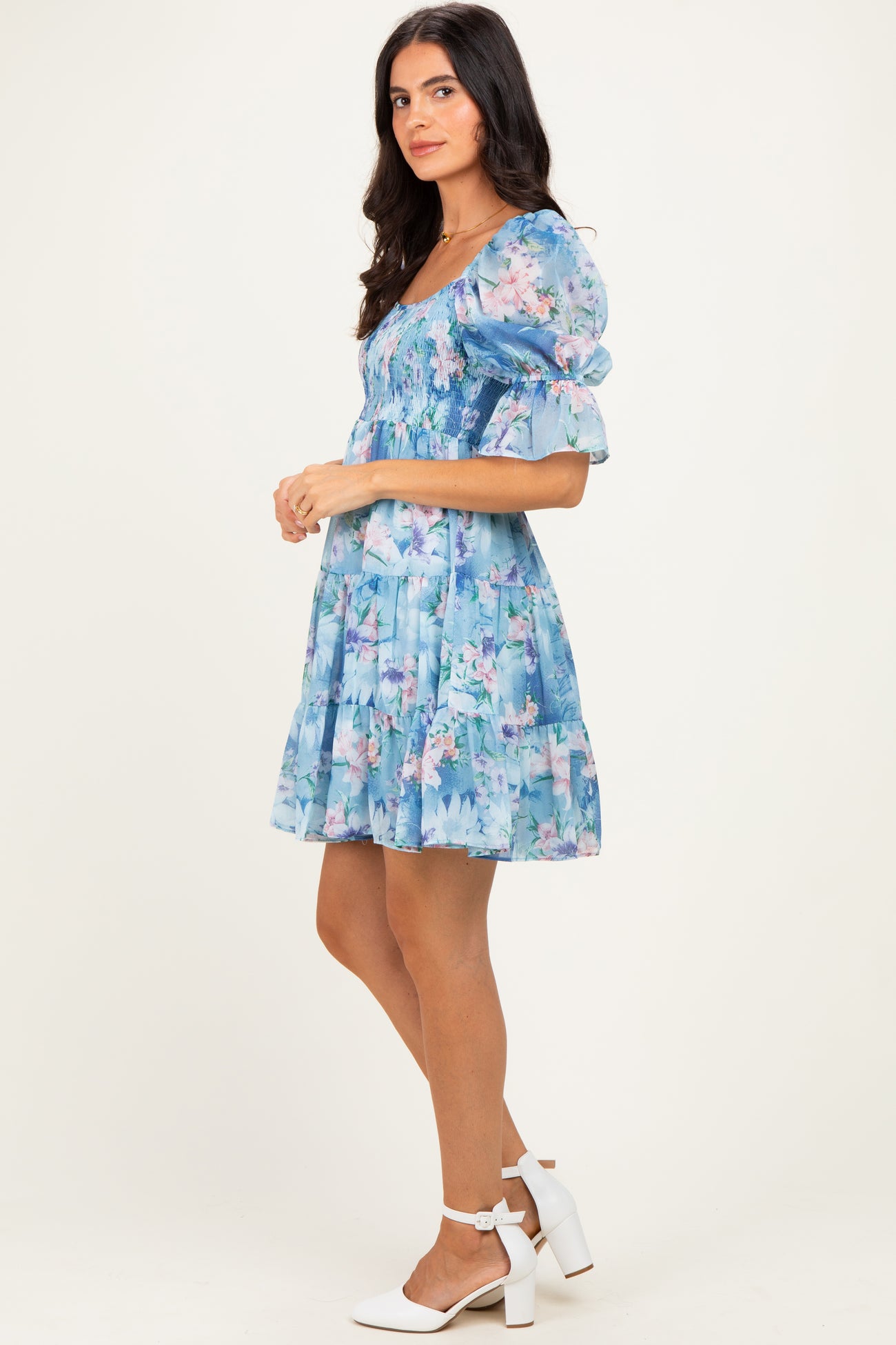 woman wearing a blue floral short sleeve dress with a ruched bodice and tiered skirt, standing in profile