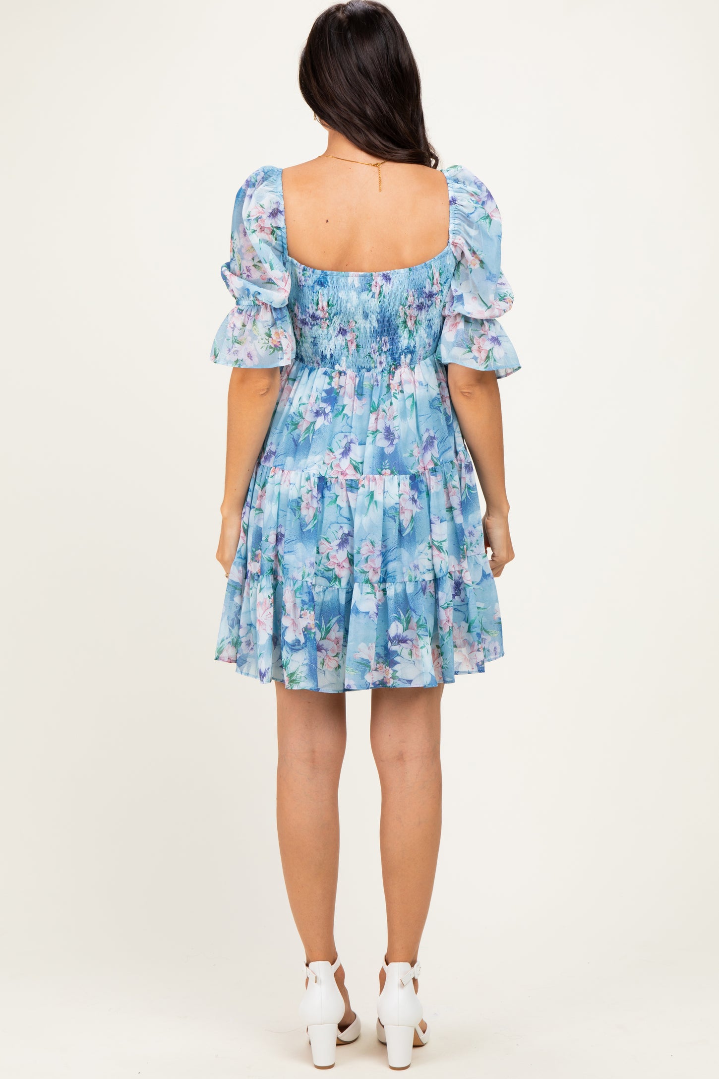 woman wearing a blue floral smocked mini dress with puff sleeves and a tiered skirt, shown from the back