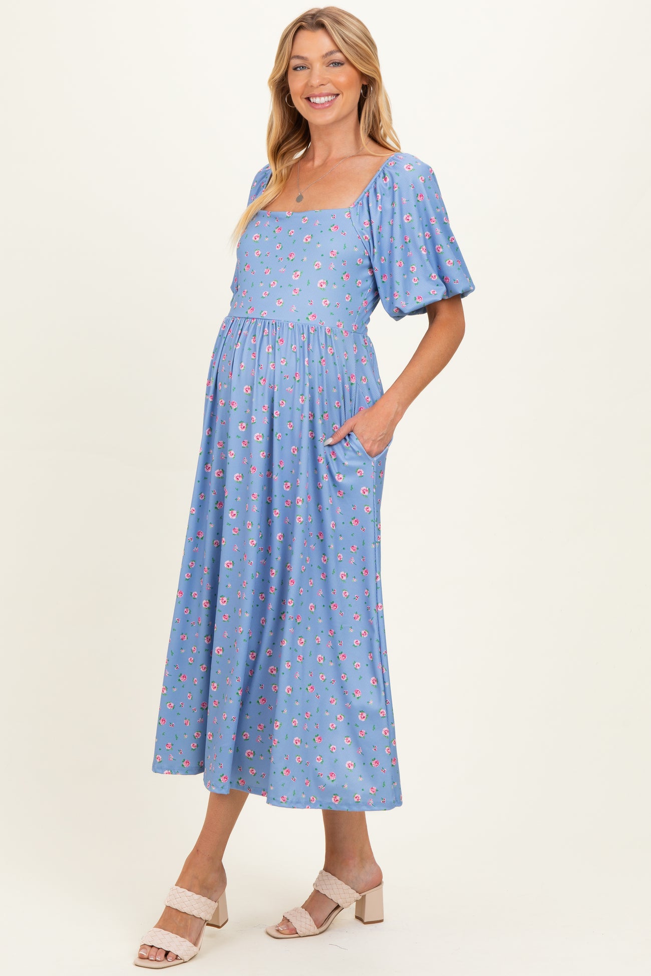 woman wearing a light blue floral maternity dress with short puff sleeves and pockets, showcasing her baby bump