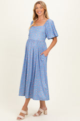 woman wearing a light blue floral maternity dress with short puff sleeves and pockets, showcasing her baby bump
