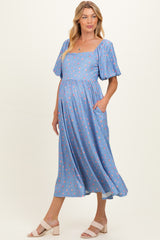 woman wearing a blue floral maternity dress with short sleeves and pockets, showcasing her baby bump
