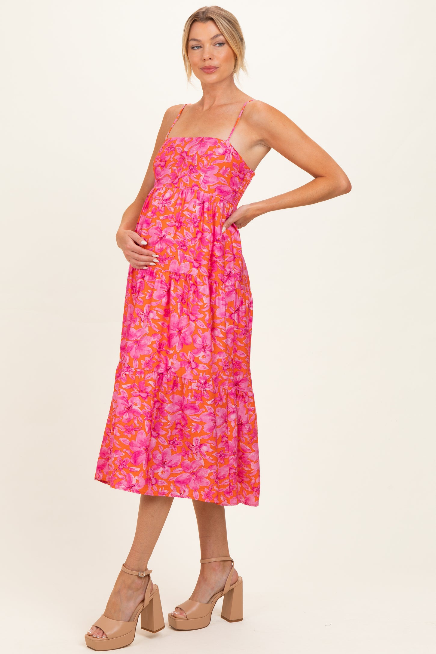woman wearing a pink floral maternity dress with spaghetti straps and a baby bump visible