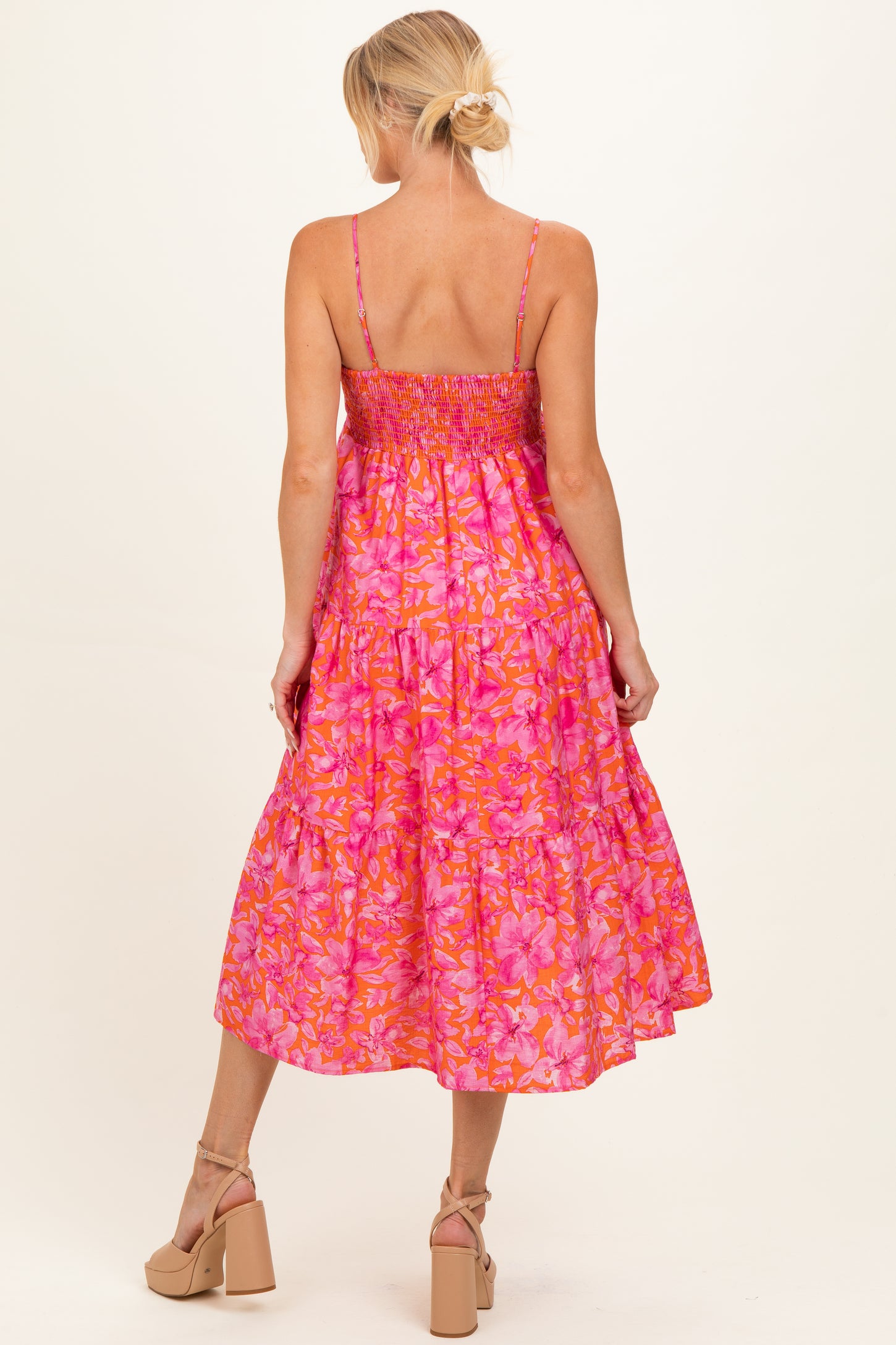 woman wearing a pink floral maternity dress with smocking and a tiered skirt, showing a baby bump from the back