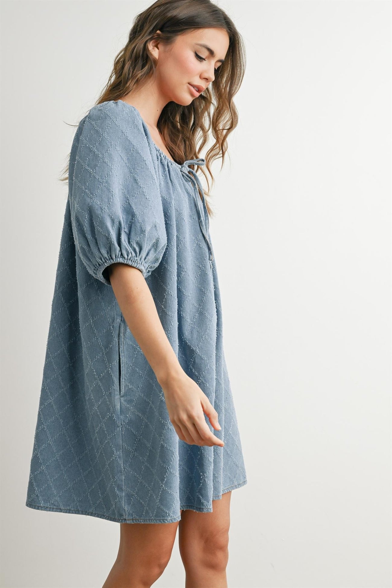 woman wearing a blue short sleeve babydoll dress with puff sleeves and tie detail at the neckline
