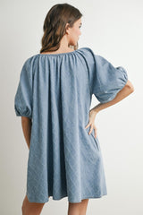 woman wearing a blue short sleeve dress with a textured pattern and puffed sleeves, viewed from the back