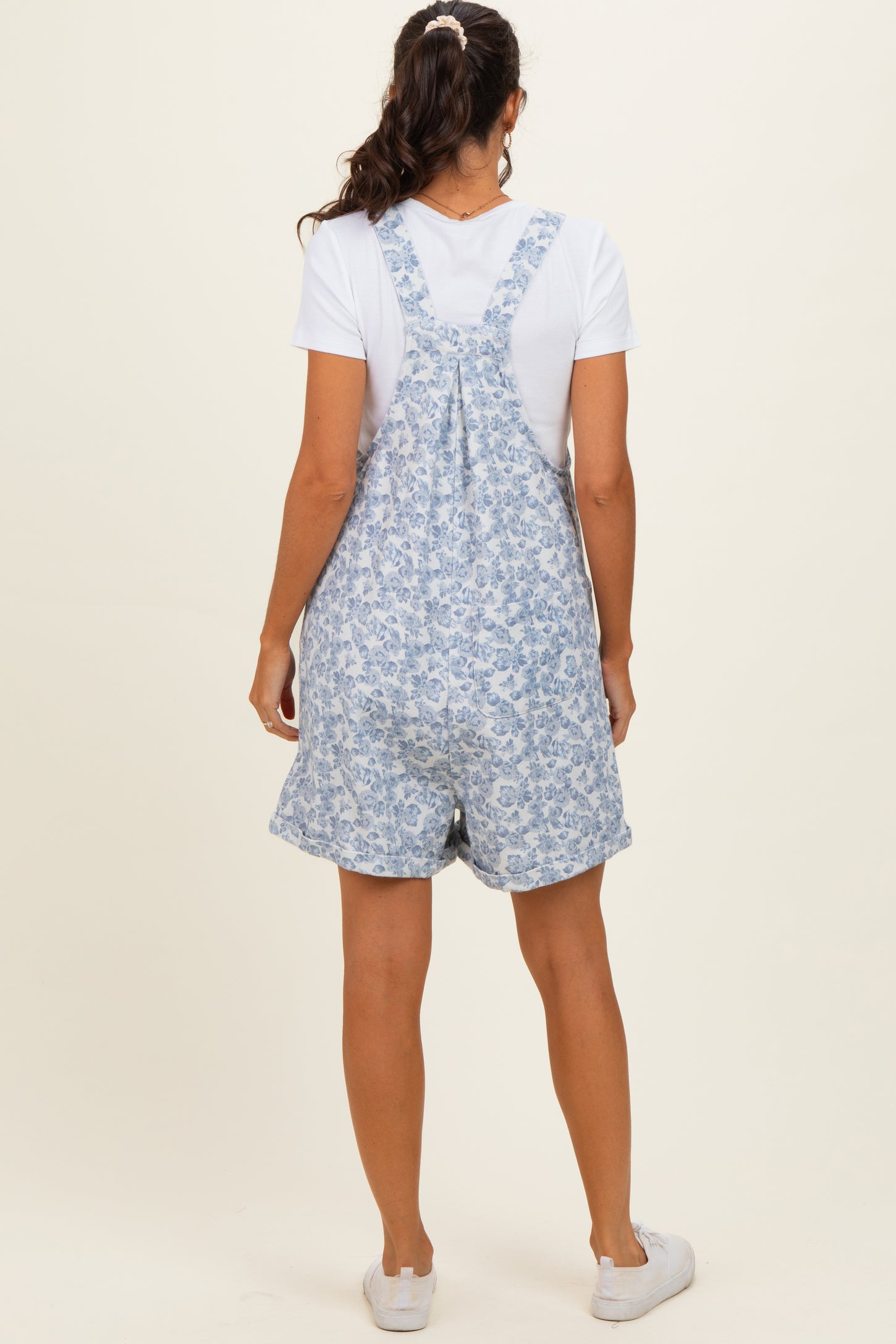 woman wearing a blue floral print overall romper with a white t-shirt underneath and white sneakers