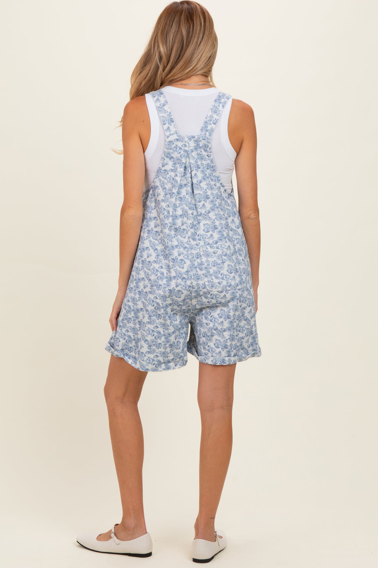 woman wearing a floral print blue maternity short overalls with a white tank top underneath and casual shoes
