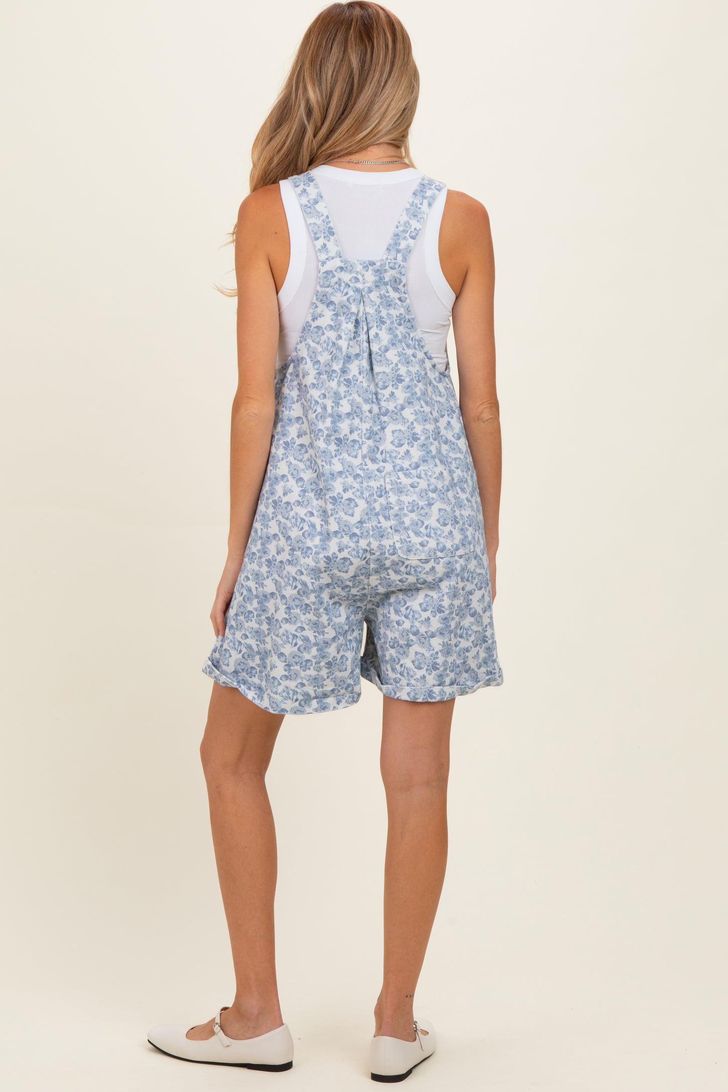 woman wearing a floral print blue maternity short overalls with a white tank top underneath and casual shoes
