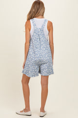woman wearing a floral print blue maternity short overalls with a white tank top underneath and casual shoes