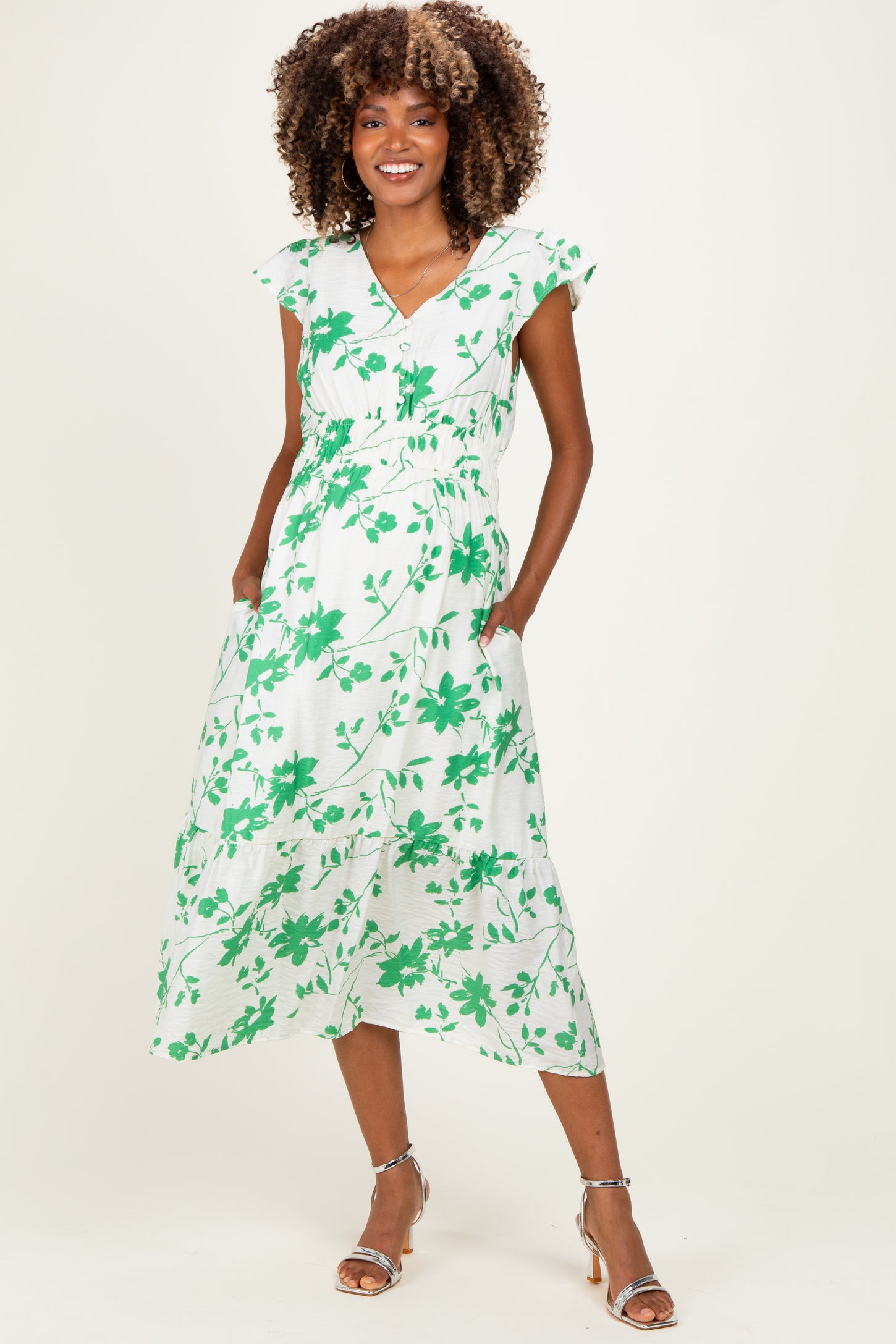 woman wearing a green floral print maternity dress with a fitted waist and pockets