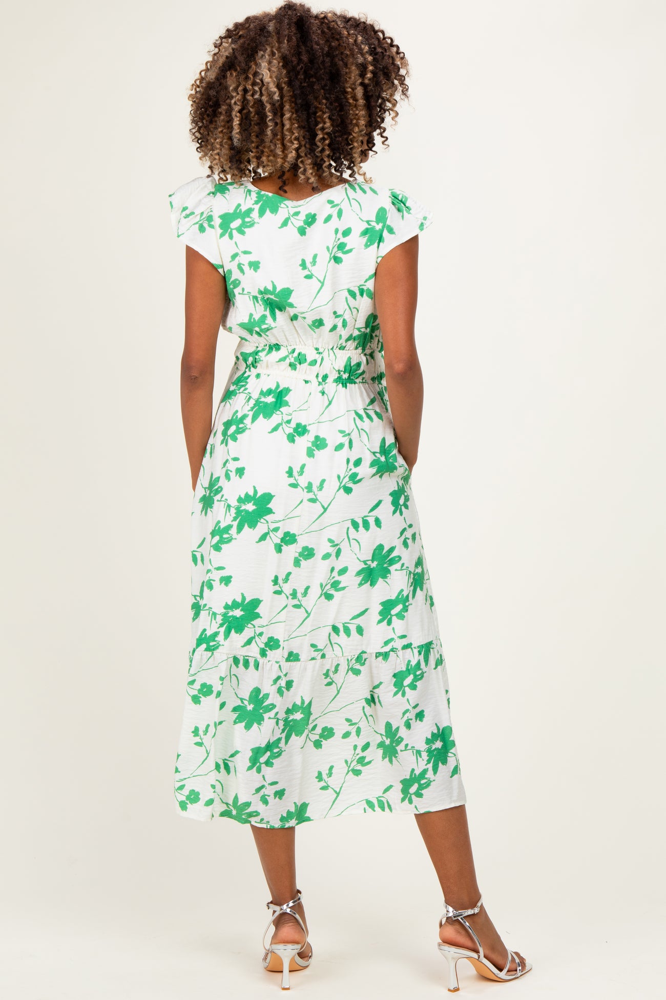 woman wearing a white maternity dress with green floral print and short sleeves, showing the back view