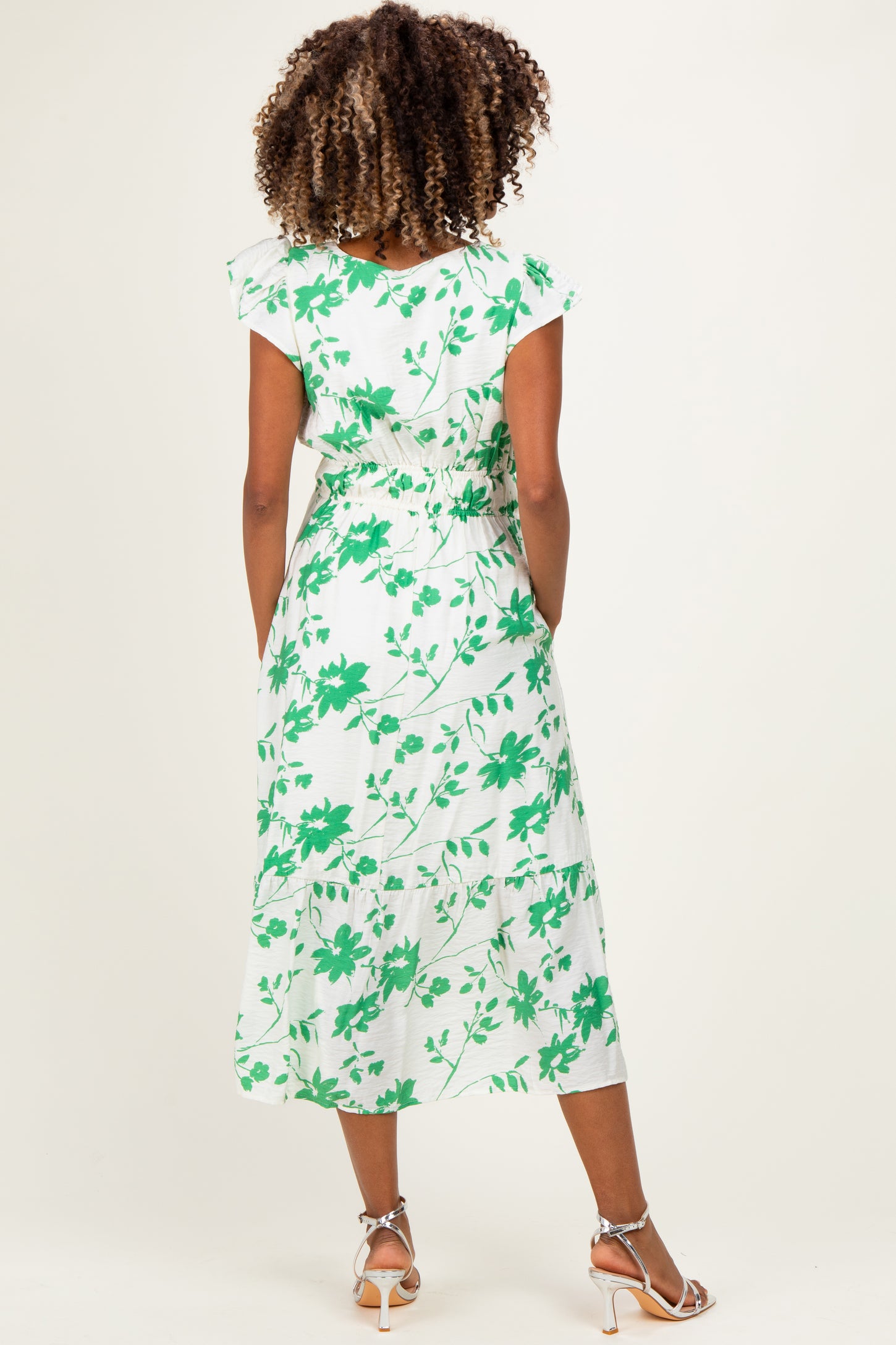 woman wearing a white maternity dress with green floral print and short sleeves, showing the back view