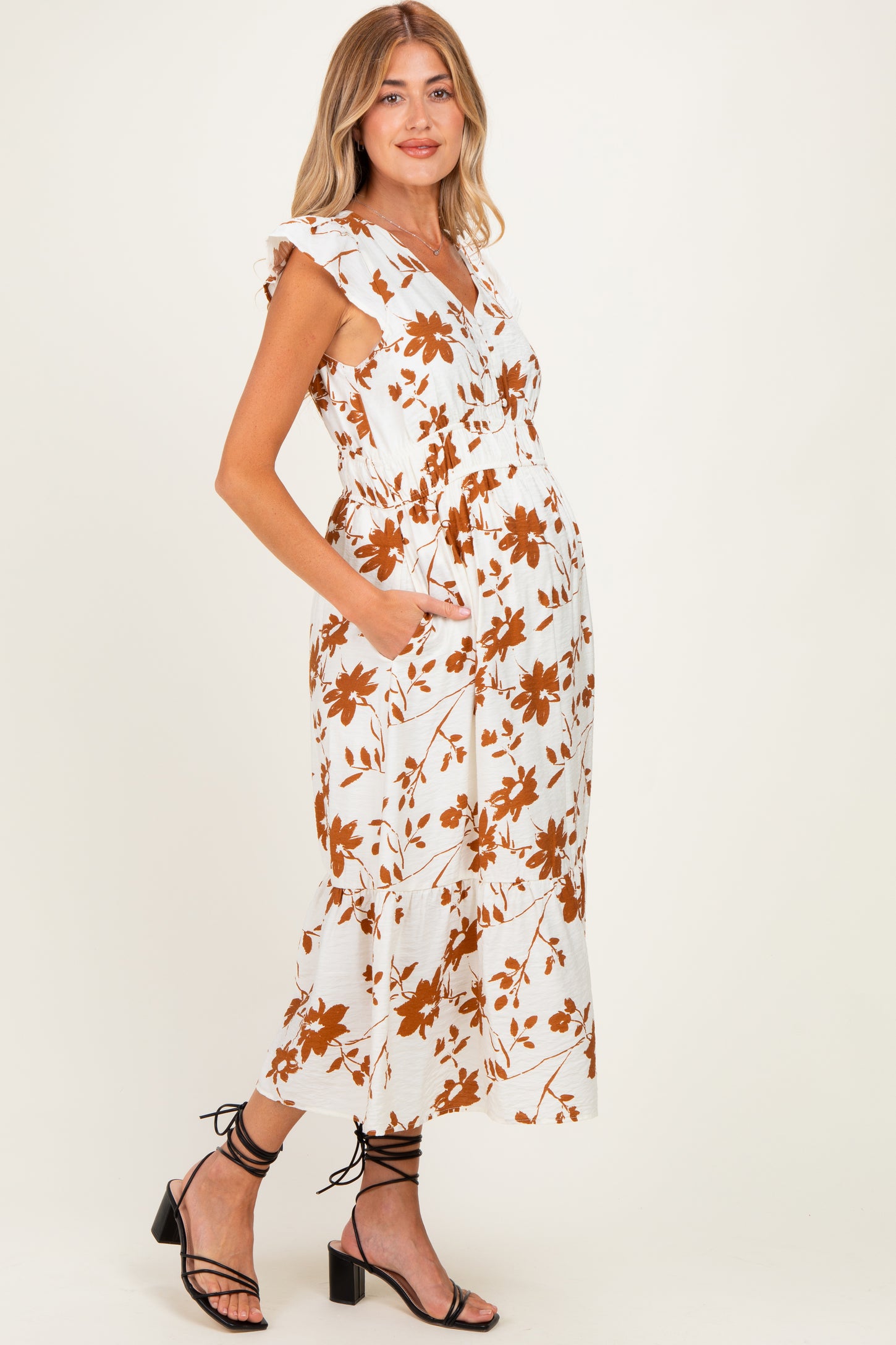 woman wearing a white floral maternity dress with ruffles and pockets, showing her baby bump