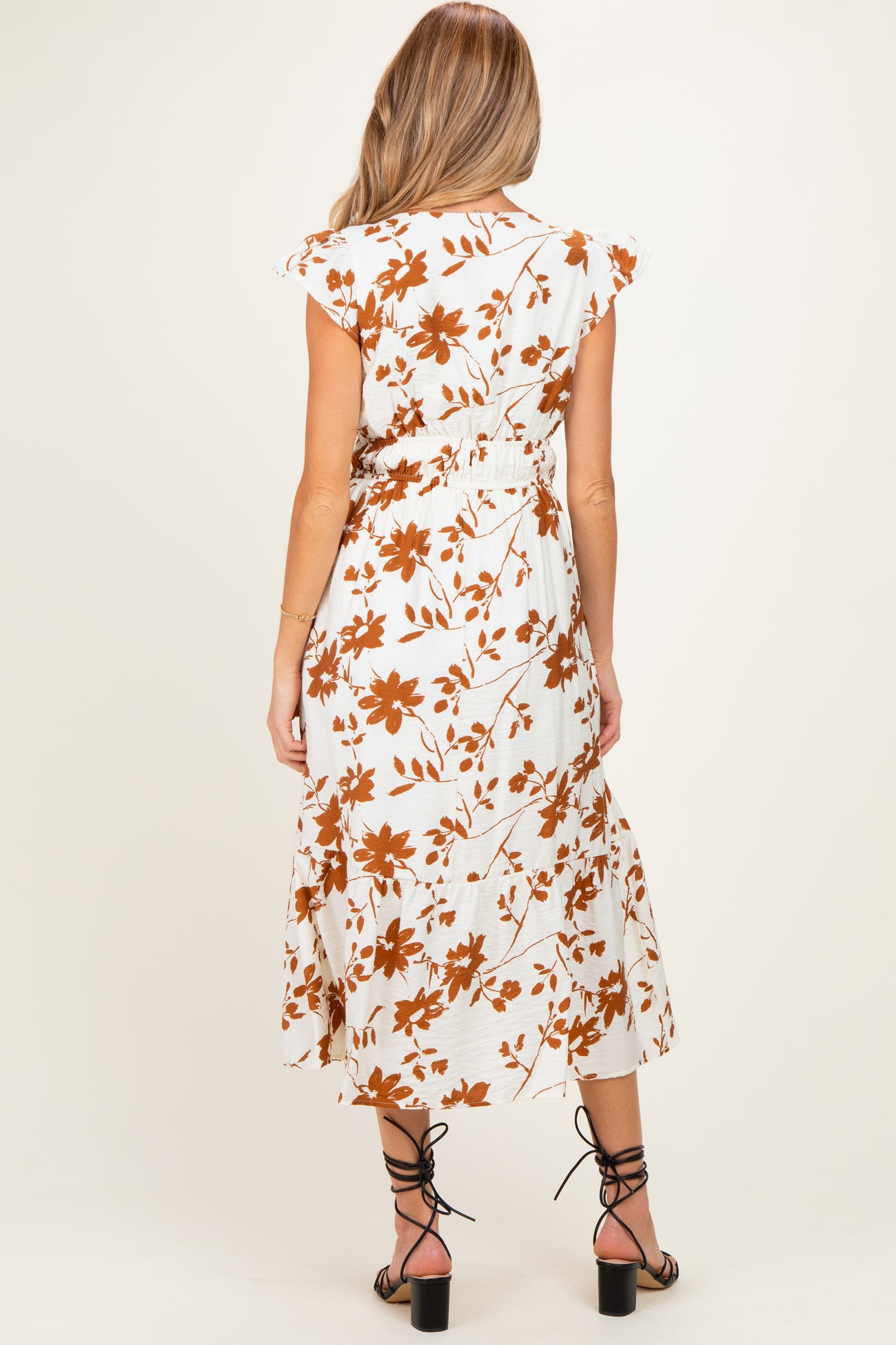 woman wearing a white maternity dress with brown floral print and flutter sleeves, showing the back view