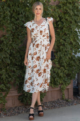 woman wearing a white floral midi dress with cap sleeves and a cinched waist, standing against a green background