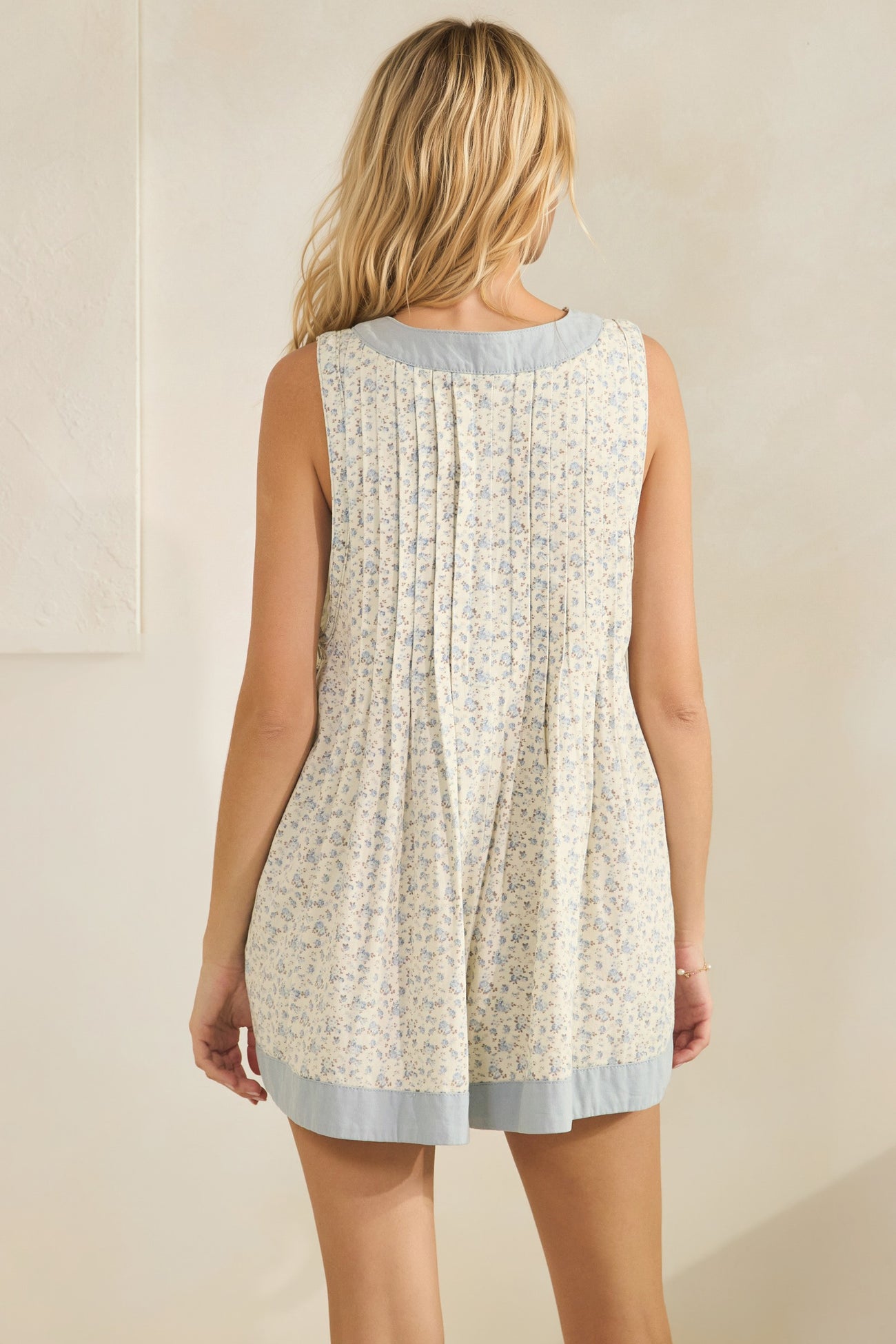 woman wearing a light yellow floral sleeveless dress with a pleated back detail