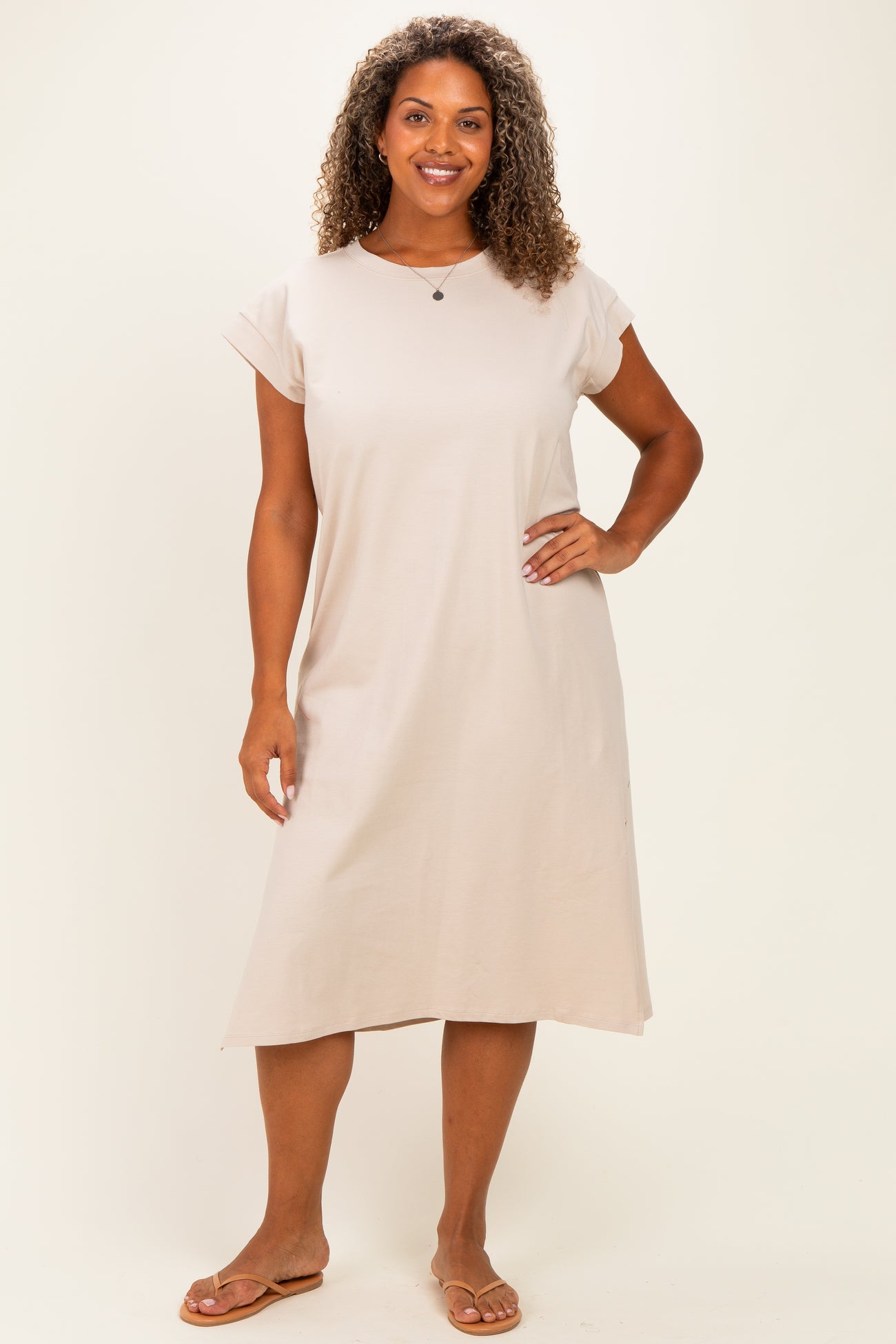 woman wearing a beige short sleeve plus size dress, standing with hands on hips and smiling at the camera