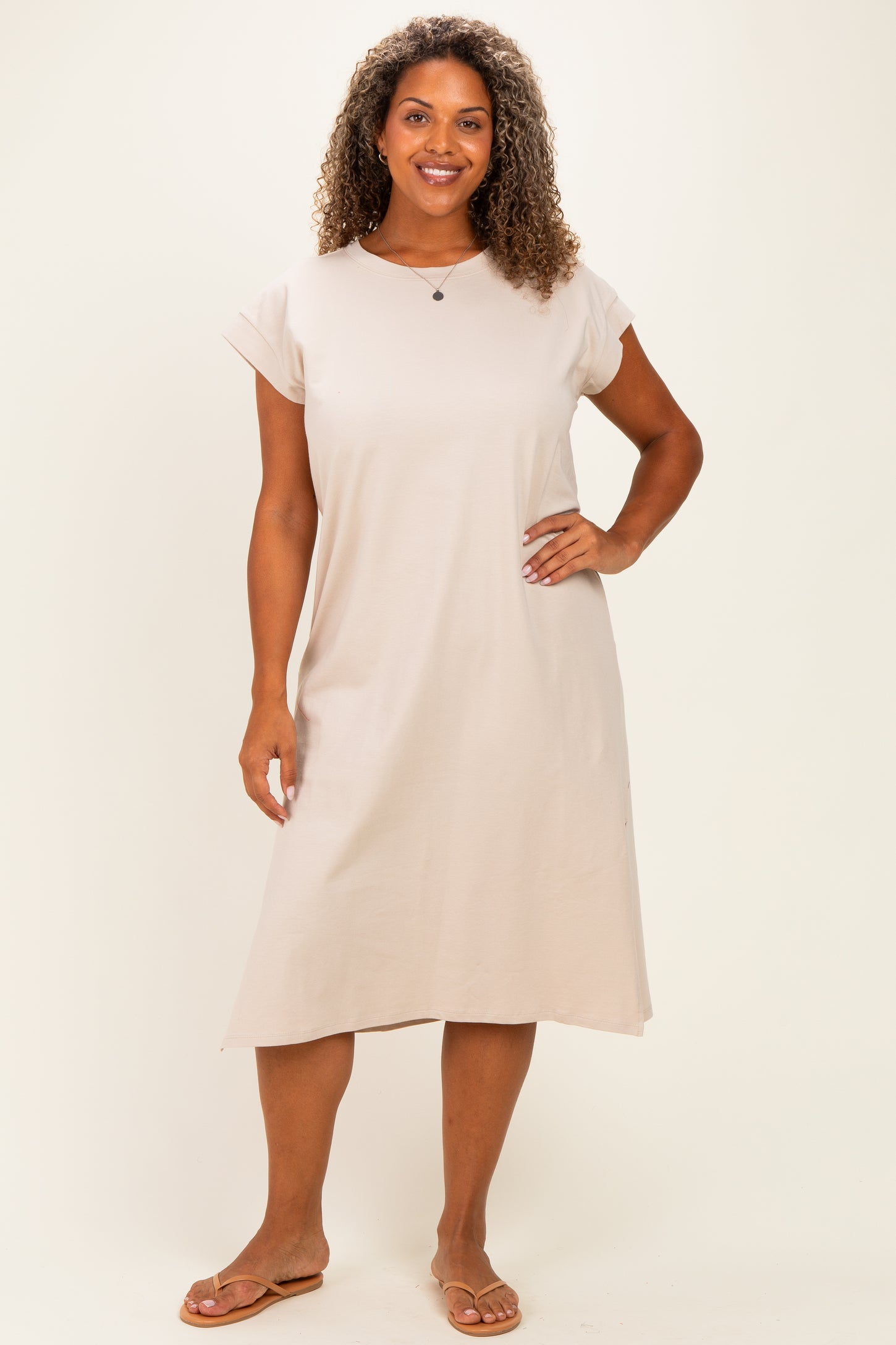 woman wearing a beige short sleeve plus size dress, standing with hands on hips and smiling at the camera