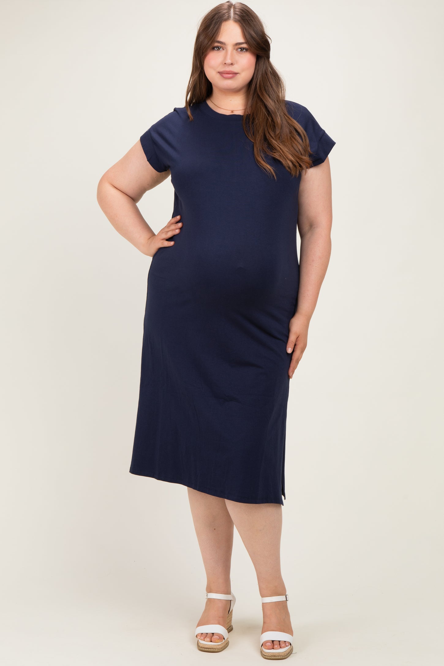 woman wearing a navy blue maternity plus dress with short cap sleeves and a relaxed fit, showcasing her baby bump