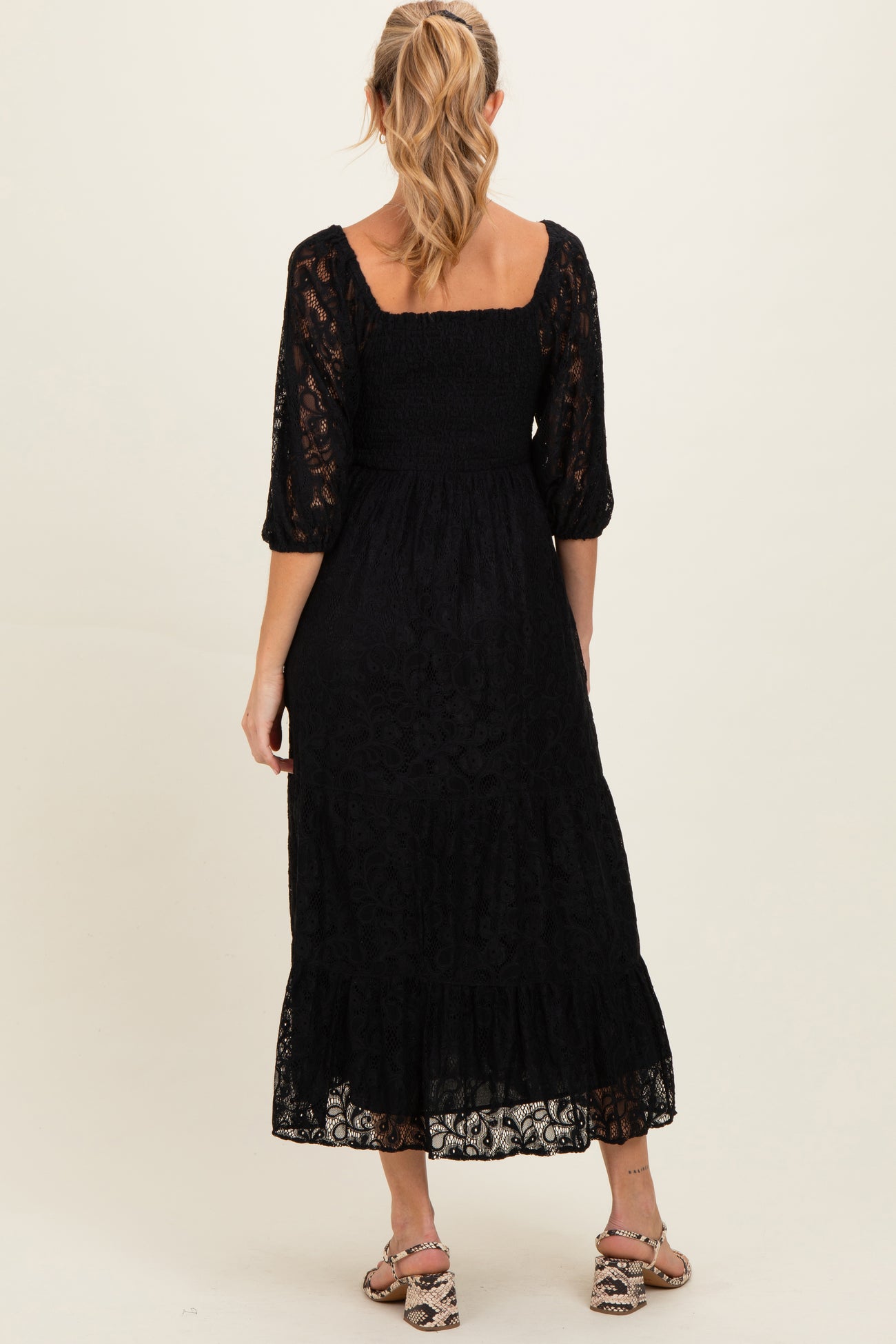 woman wearing a black lace maternity dress with a smocked bodice and three-quarter sleeves, showing a flowing skirt