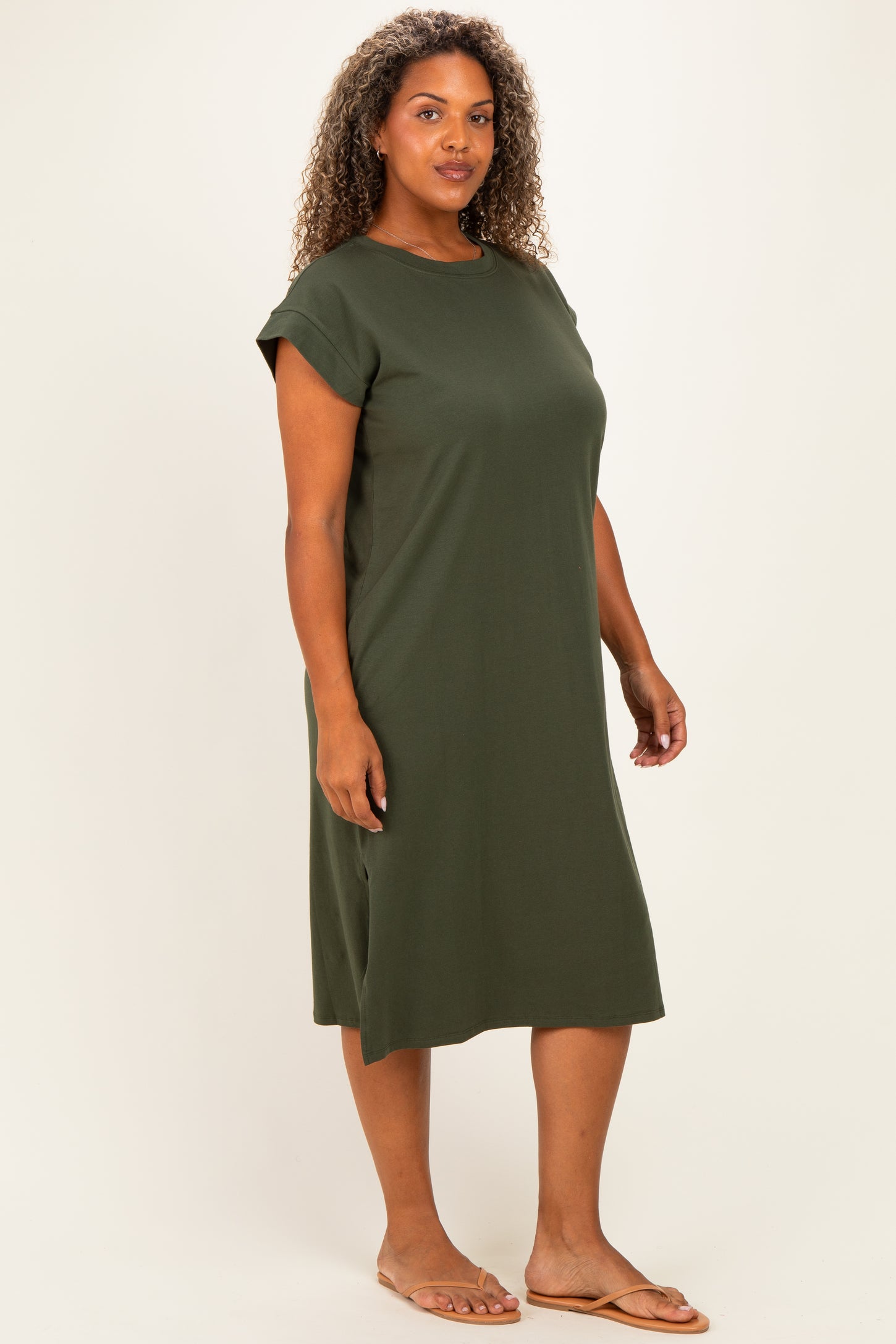 woman wearing a dark green short sleeve plus size dress with a relaxed fit and side slits, standing sideways in sandals