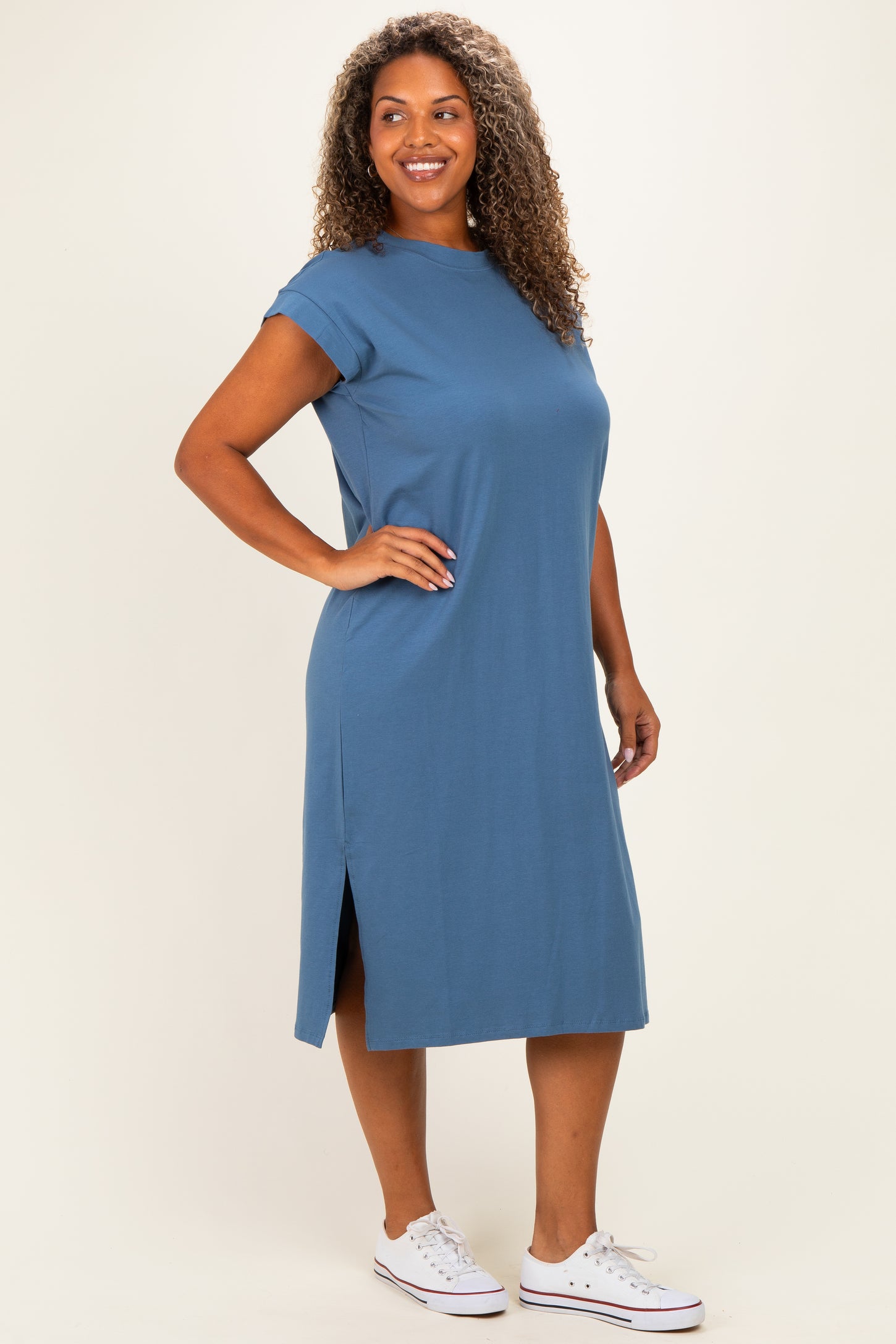 woman wearing a relaxed fit blue midi dress with short sleeves and side slits, paired with white sneakers