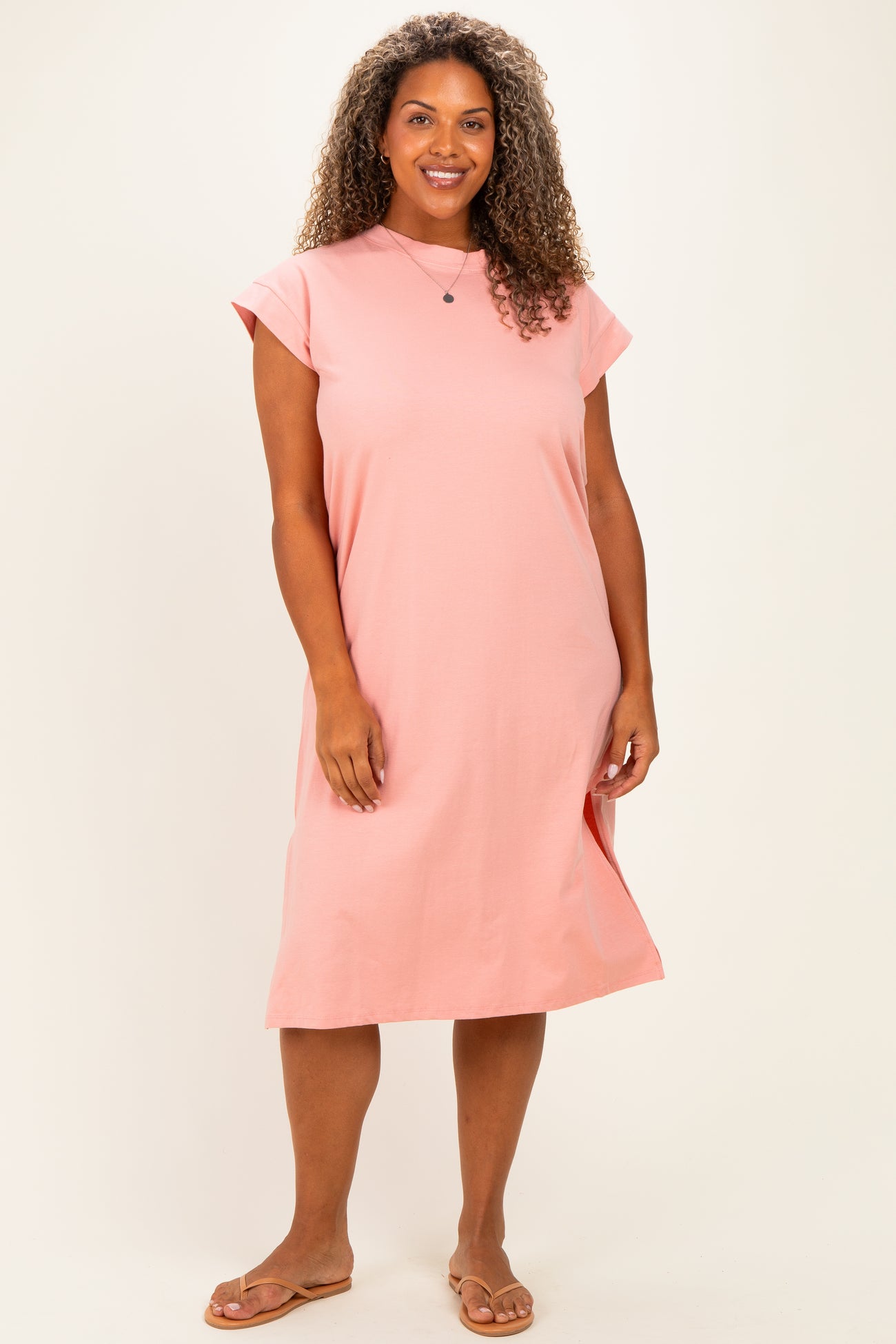 woman wearing a pink short sleeve plus size dress with a relaxed fit and side slits, standing and smiling
