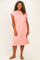 woman wearing a pink short sleeve plus size dress with a relaxed fit and side slits, standing and smiling