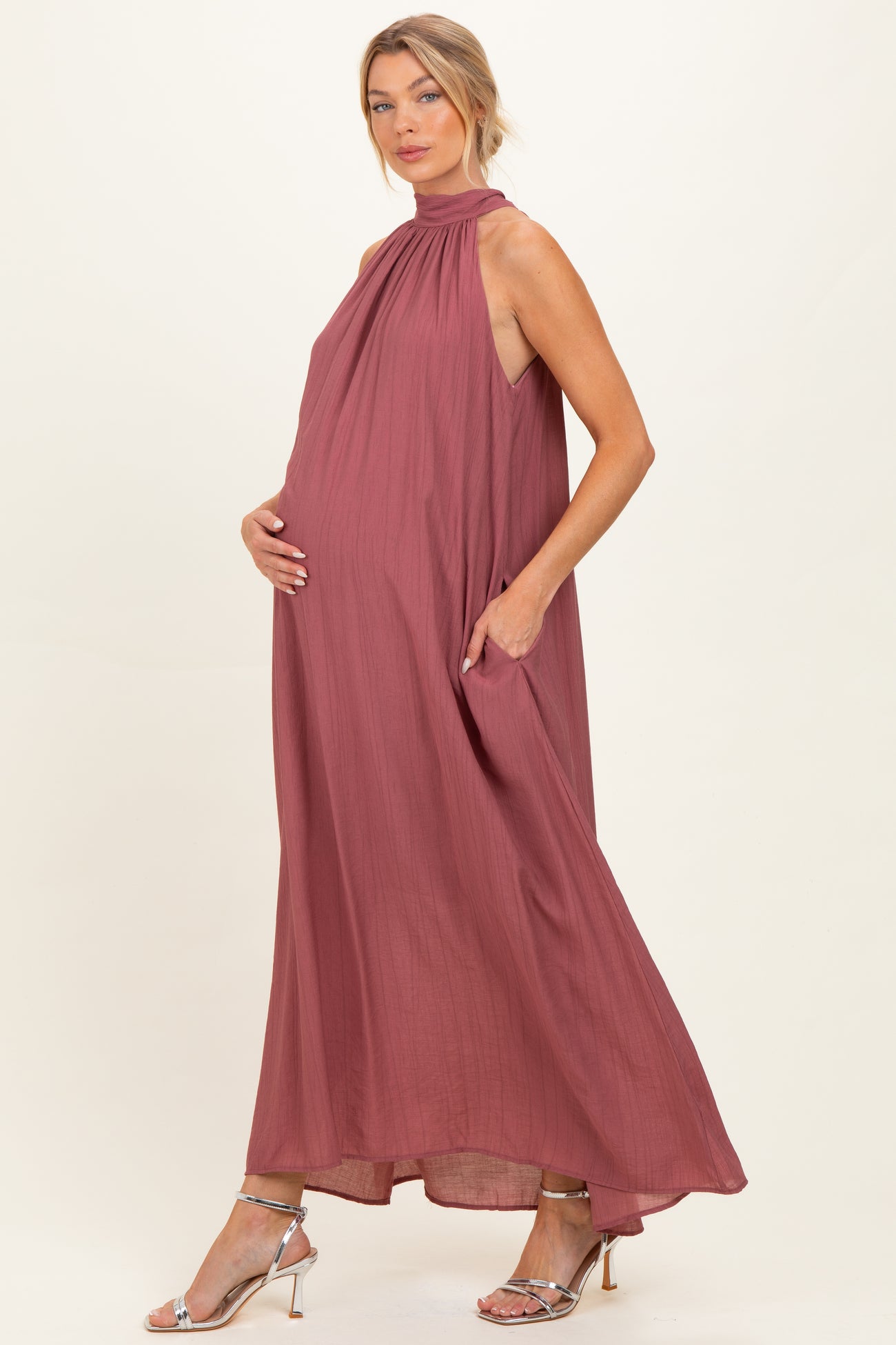 woman wearing a dusty rose sleeveless maternity dress with a high neck and pockets, showcasing her baby bump